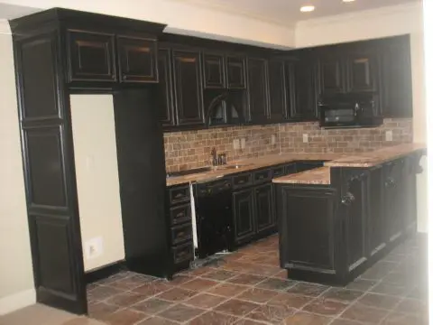 A kitchen with black cabinets and brick walls.