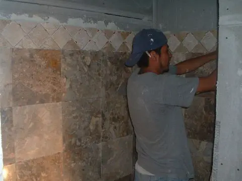 A man in a hat is working on the wall of a bathroom.