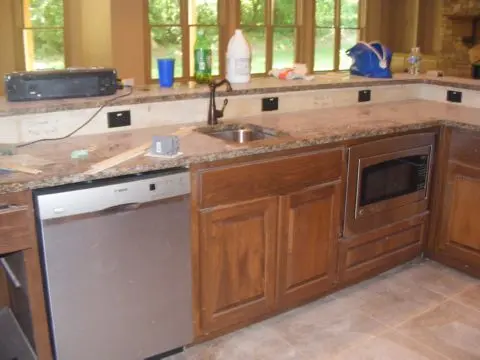 A kitchen with brown cabinets and marble counter tops.