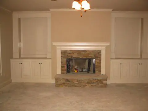 A fireplace in the middle of a room with white cabinets.