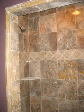 A tiled shower with a marble tile wall.