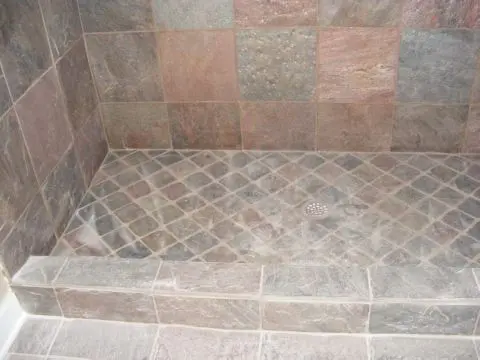 A tiled shower with a stone floor and walls.