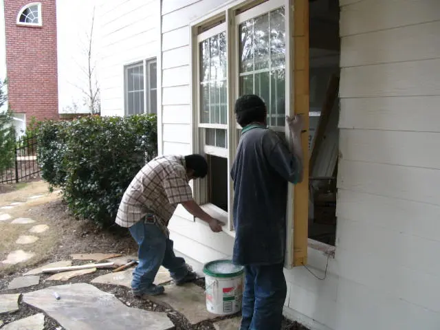 Two men are painting a window on the outside of a house.