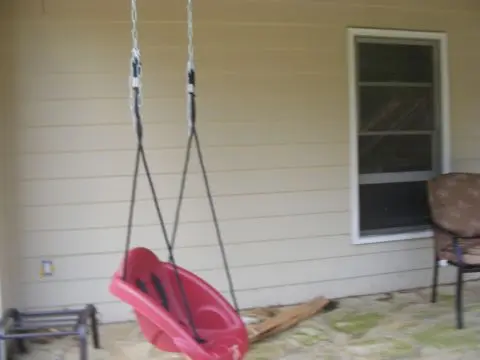 A red plastic swing set in front of a house.